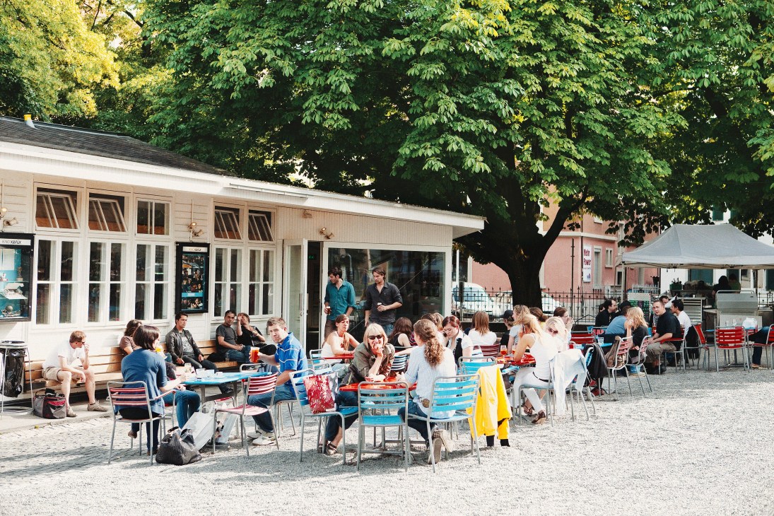 Outdoor café terrace with diners seated at tables under trees in Zürich