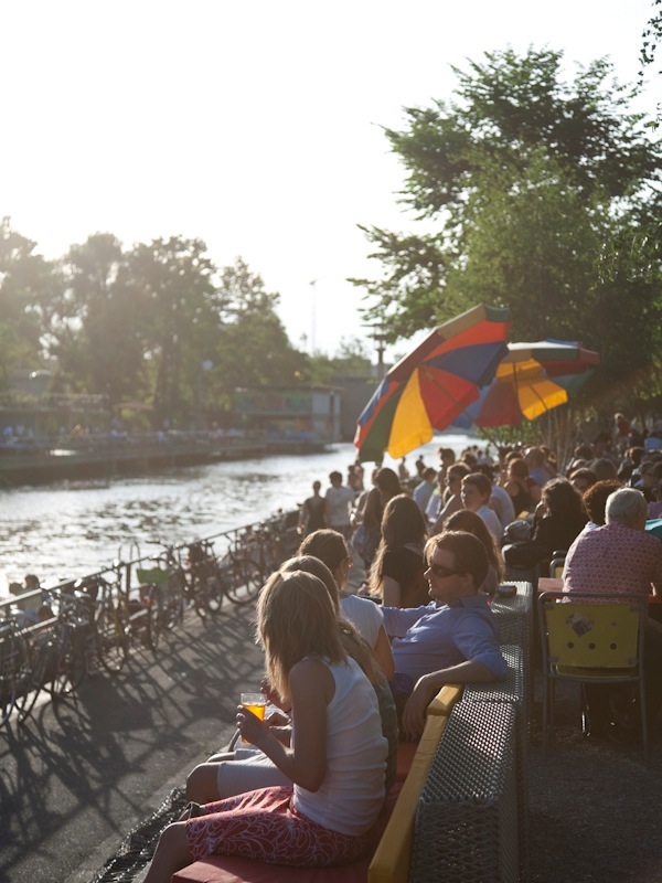 People sitting along a waterside with colorful umbrellas on a sunny day in Zürich.